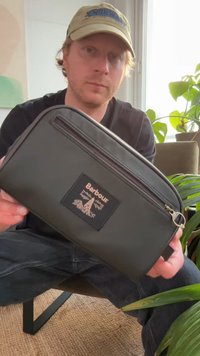 Necessaire preta com fecho de correr, feita de material texturizado, apresentando um patch com o logótipo proeminente da Barbour, fecho de correr metálico e formato elegante.