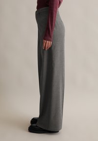 Szare spodnie w paski o szerokich nogawkach z wysokim stanem, wykonane z miękkiego materiału i o luźnym kroju, w połączeniu z czarnymi butami na platformie.