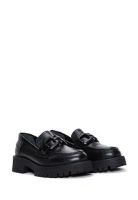 Schwarze Lederschuhe mit einer massiven Plattformsohle, die über eine dekorative Schnalle und kontrastierende Nähte entlang der Kante verfügt.