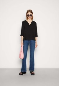 Top nero a V con maniche a tre quarti, jeans svasati blu, sandali con piattaforma nera spessa e borsa intrecciata rosa.