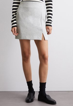 Mini-jupe en tissu extensible gris clair avec une fente latérale et une taille plate. Associée à un haut à rayures noir et blanc à manches longues et à des chaussures noires.