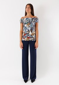 Top scollato con stampa floreale nei toni di blu, verde e arancione, abbinato a pantaloni larghi blu scuro e scarpe nere con punta.