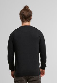 Suéter negro de punto con mangas largas, puños acanalados y un cuello redondeado. Textura suave, diseño minimalista y un corte ligeramente holgado en la parte de atrás.