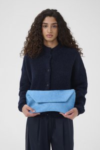 Pochette en fourrure bleue avec un rabat angulaire tenue à la main, assortie à un pull texturé foncé avec un col et des boutons.