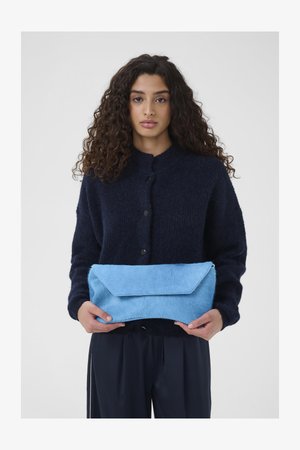 Blue fur clutch bag with an angular flap design held in hands, paired with a dark textured sweater featuring a collar and button closures.