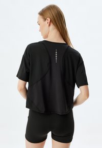 Mustat lyhythihaiset urheilu paita, jossa on ainutlaatuinen selkädesign. Paita on sileä ja siinä on heijastava pistekuvio yläselässä.