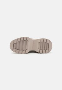 Sål af en beige Michael Kors sko med dybe spor og riller for greb, sat mod en plain hvid baggrund.