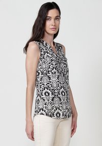 Blusa senza maniche in bianco e nero, caratterizzata da un'elegante fantasia floreale, design a scollo a V e una texture setosa. Vestibilità sartoriale con orlo curvo.