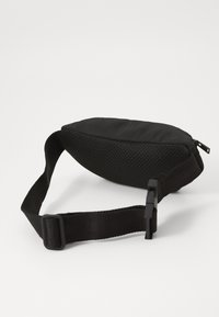 Sac banane noir avec un design arrondi, fabriqué en tissu lisse et en texture en maille. Dispose d'une boucle à déclenchement latéral et d'une fermeture éclair.