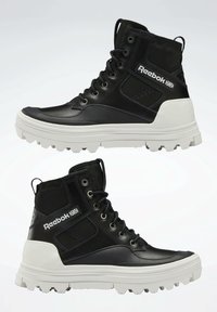 Black high-top boots with a smooth leather and mesh design, featuring a thick white sole and prominent Reebok logo on the side.