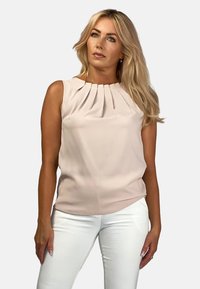 Jasnoróżowa bluzka bez rękawów z plisowanym przodem, miękka tkanina i okrągły dekolt, zestawiona z białymi dopasowanymi spodniami.