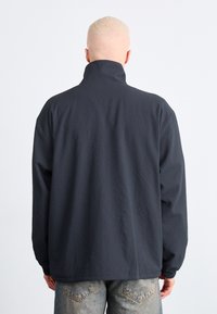 Giacca collare grigia scura con tessuto testurizzato, maniche lunghe e vestibilità rilassata. Presenta polsini elasticizzati e un design semplice.