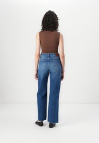 Blauwe high-waisted jeans met een rechte pijp, grote achterzakken en een tan leren label op de tailleband. Bruine aansluitende tanktop.