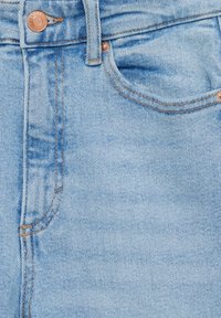 Tela de denim azul claro de unos vaqueros con vista de cerca, que presenta costuras visibles, un cierre de botón y un detalle de bolsillo delantero.