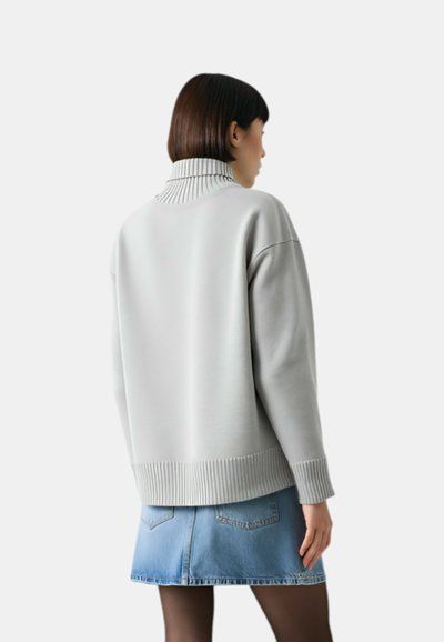 Maglione oversize color grigio chiaro con colletto e polsini a costine, abbinato a una gonna di jeans. Texture morbida e vestibilità rilassata.