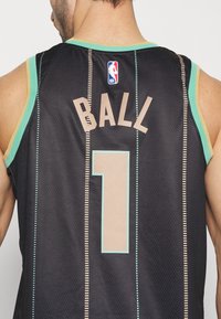 Maillot de basket-ball noir avec des accents verts, en tissu mesh, avec "BALL" et le numéro "1" en beige, et un petit logo NBA sur l'épaule.