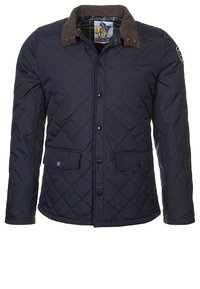 Marineblau gesteppte Jacke mit braunem Cordkragen, Frontknopfverschluss, zwei Klappentaschen und kariertem Futter. Verfügt über ein kleines Logo am Ärmel.