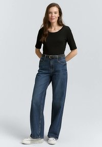 Black short-sleeve top paired with high-waisted, wide-leg blue denim jeans and white sneakers, featuring a classic belt for added detail.