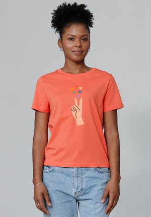 T-shirt à manches courtes corail en coton, arborant un symbole de paix avec un geste de la main et des cœurs colorés au-dessus. Col rond simple et coupe décontractée.