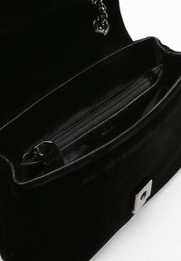Interno della borsa in velluto nero con un compartimento con zip e hardware argentato. Texture morbida, forma rettangolare e dettaglio della tracolla a catena.