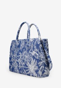 Bolso tote de patrón floral azul hecho de tela texturizada; cuenta con dos asas, una correa desmontable y un interior espacioso para transportar objetos.
