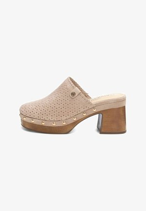 Zoccolo sintetico beige con design perforato, tacco in legno e borchie dorate lungo la suola. Stile con retro chiuso e punta aperta.