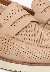 Světlé béžové kožené boty s perforovaným vzorem a plochou podrážkou. Obsahují široký, plochý pásek přes svršek. Detaily s kontrastním prošíváním.