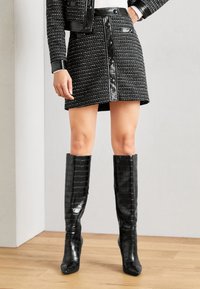 Zwarte tweed minirok met leren accenten en knoopsluiting, gecombineerd met zwarte croco-geemboste kniehoogte laarzen met spitse neuzen.