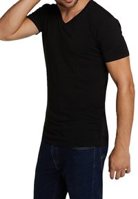 T-shirt nera in cotone con collo a V e maniche corte, design aderente, texture liscia e dettagli di cucitura minimi. Indossata con jeans in denim blu.