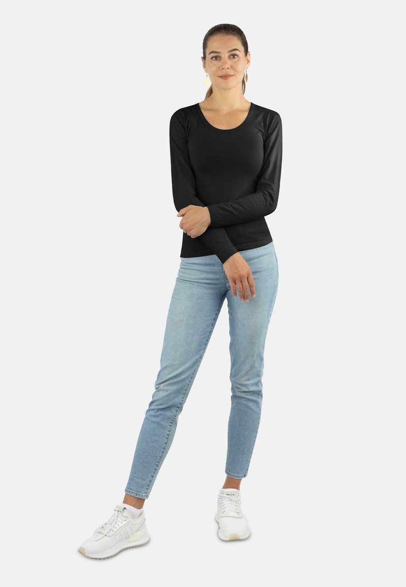 Schwarzes Langarmshirt mit rundem Ausschnitt und glatter Textur, kombiniert mit hellblauen Slim-Fit-Jeans und weißen Sportschuhen.