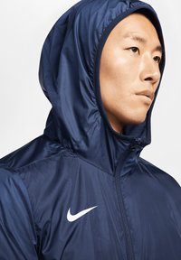 Marineblauwe hoodie met een gestructureerd oppervlak, met een wit Nike-logo op de linkerborst en een ritsdetail aan de voorkant.