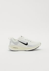 Hvid sportsko med en åndbar mesh-overdel, sort Swoosh-logo og en tykk cremede sål med "zoomx" branding.