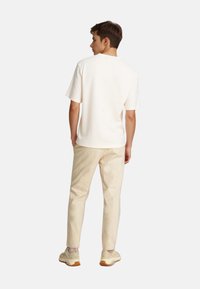 Off-white t-shirt med kort ærme, rund hals, parret med lysebeige bukser og cremede sneakers. Glat tekstur, afslappet pasform.