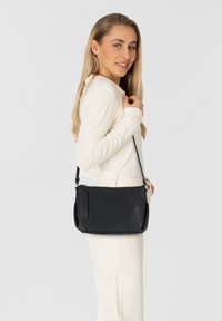 Bolso de hombro de cuero negro con acabado texturizado, bolsillo con cremallera, correa ajustable y forma rectangular compacta.