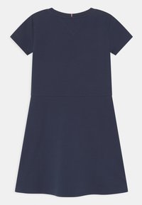 Granatowa sukienka z krótkim rękawem, wykonana z gładkiej tkaniny, z dopasowaną górą i rozkloszowanym dołem, z delikatnym wcięciem w kształcie litery V przy dekolcie.
