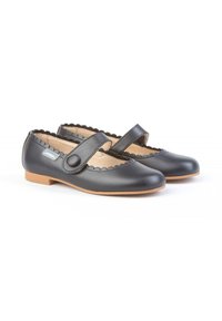 Zapatos Mary Jane de cuero negro con bordes ondulados, punta redonda y suela plana de goma marrón. Asegurados con una correa negra y detalle de botón.