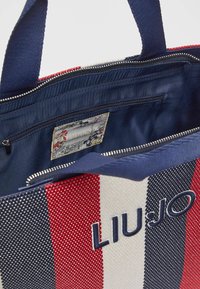 Sac rayé en rouge, blanc et marine. Confectionné en tissu texturé avec deux poignées, poche intérieure zippée et étiquette de marque à l'intérieur. Fermeture éclair.