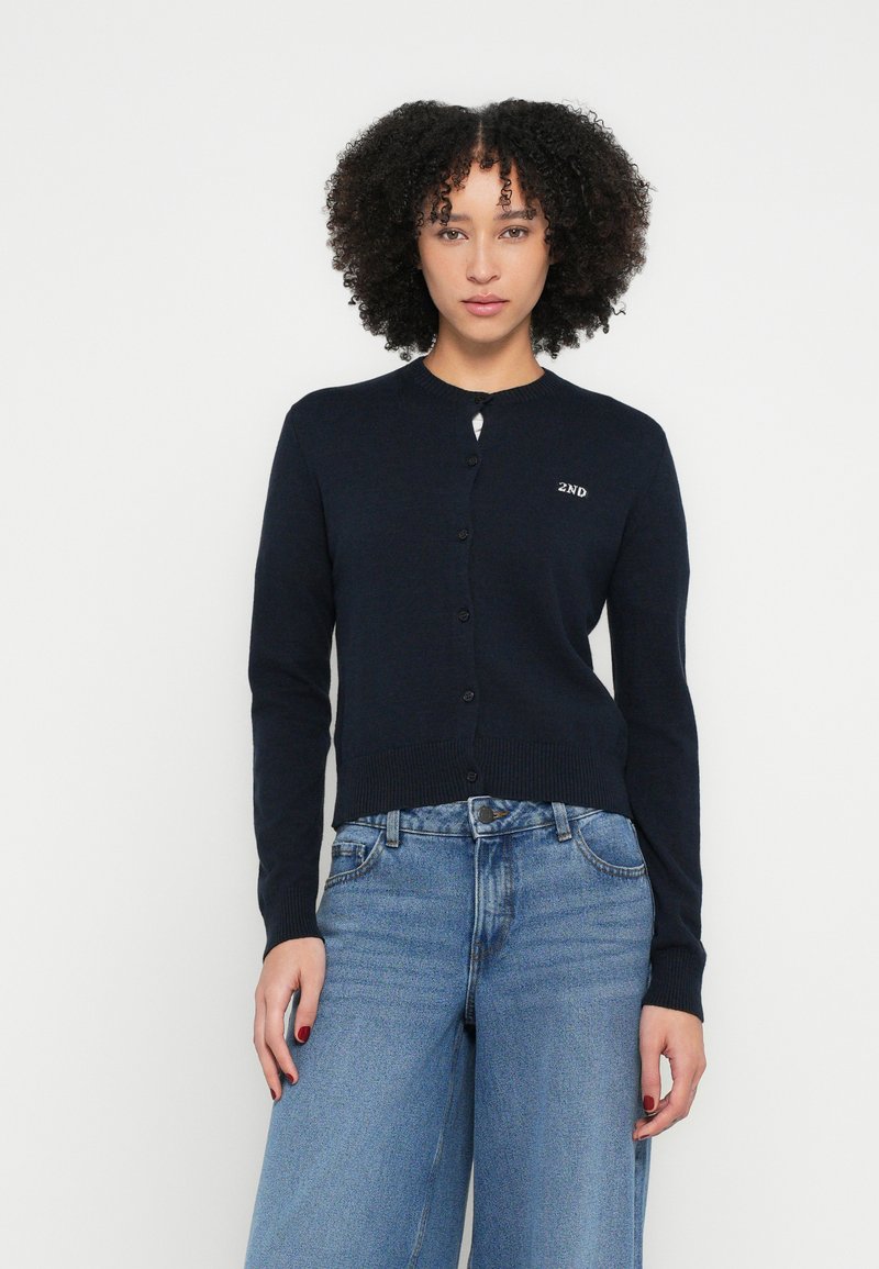 Tumši zils kardigans ar apaļu kakla izgriezumu, garām piedurknēm un poga uz priekšu. Kreisajā pusē izšūts "2ND" logotips. Mīksta tekstūra.