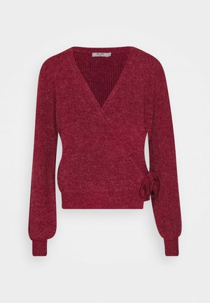 Pull cache-cœur rouge en maille à manches longues avec col en V et détail nœud sur le côté, texture côtelée et poignets ajustés.