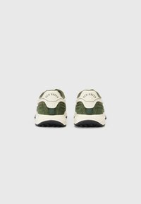 Tenisi din suede verde cu accente albe, având un design curbat, o talpă texturată și inscripția "NEW HAVEN" pe spate.