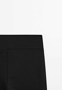 Legging noirs avec une taille élastique lisse. Le tissu a une finition mate et des détails de couture minimaux sur la taille.