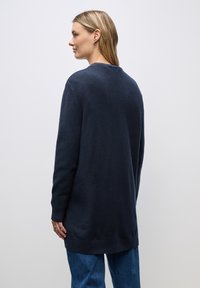 Długi granatowy sweter z miękkiej dzianiny, z okrągłym dekoltem i ściągaczami na końcach rękawów, sięgający poza biodra, zapewniający luźny krój.