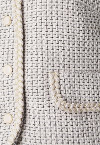 Biały żakiet z tkaniny tweed z teksturowanym wzorem, ozdobiony złotymi, plecionymi wykończeniami wzdłuż brzegów oraz okrągłymi guzikami.