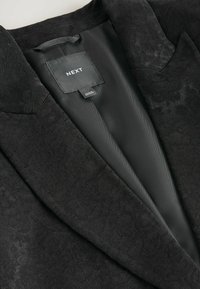 Black blazer featuring a textured floral pattern, satin interior, notch lapels, and "NEXT" label sewn inside.