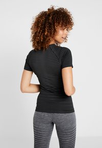 Black short-sleeve athletic top with a textured striped pattern, paired with gray striped leggings, emphasizing a fitted design.