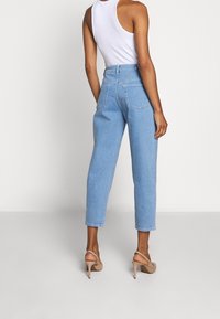 Vaaleansiniset korkeavyötäröiset farkut, joissa on kapeneva malli, etutaskut ja sileä denim-kangas, yhdistettynä beigeihin korkokenkiin.