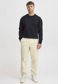 Hanorac negru cu un logo subtil, pantaloni crem și adidași albi cu un detaliu cu model. Design simplu și croială lejeră.