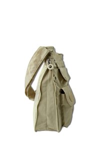 Sac en toile beige avec une fermeture éclair, une sangle ajustable, une poche frontale et un détail de logo en relief. La texture semble douce et durable.