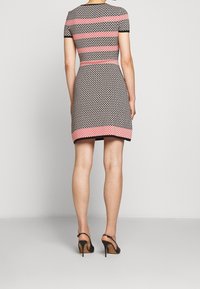 Robe ajustée à manches courtes avec un motif géométrique noir et blanc, ornée de rayures roses et d'un ourlet uni, associée à des chaussures à talons noirs.