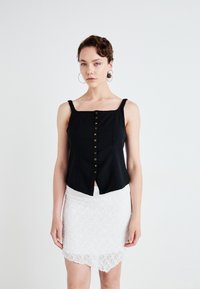 Svart kort tanktopp med knappdetalj foran, kombinert med en hvit lace mini skjørt med bølget kant.